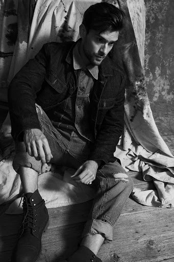 A portrait shot of an adult male with a focused expression, captured in a photo studio with soft, diffused lighting and a grey backdrop.