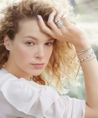 Close up portrait of a woman with curly blonde hair wearing layered diamond rings, tennis bracelets, and stud earrings.