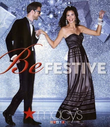 A smiling woman in a strapless black evening gown dancing with a man in a black tuxedo against a sparkly silver backdrop.
