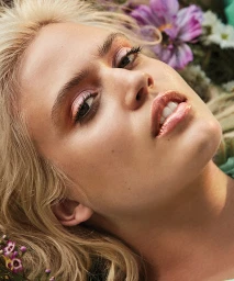 Close up portrait of a blonde woman with pink eyeshadow and glossy lips surrounded by flowers styled by Forest Watson