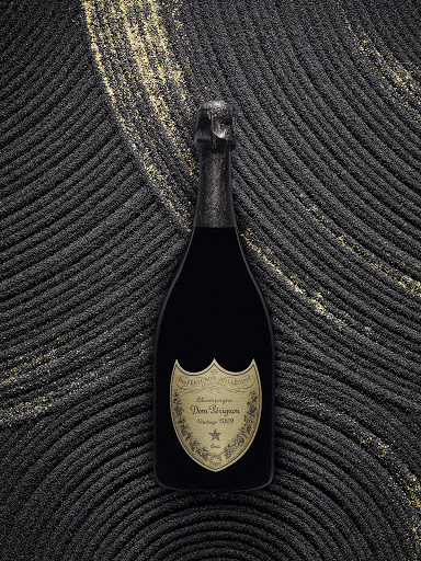 Black Dom Perignon champagne bottle on a dark, textured surface with gold accents, presented in a studio setting with soft lighting.