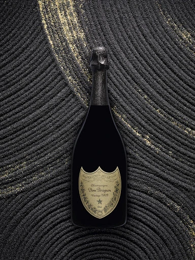 Black Dom Perignon champagne bottle on a dark, textured surface with gold accents, presented in a studio setting with soft lighting.