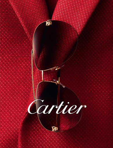 Sunglasses with gold frames are displayed over a textured red jacket. The brand name, Cartier, is displayed across the lenses.