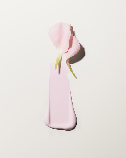 Close-up of a pink cream stroke with a pink flower petal on a cream background, highlighting textures and subtle shadows.