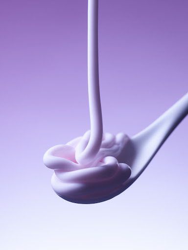 Pink cream being poured onto a white spoon against a gradient purple background, showcasing a beauty or food product texture.