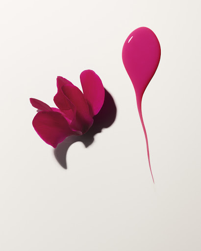 Overhead shot: vibrant pink petals cascade on a white backdrop beside a teardrop-shaped paint splash, creating an organic beauty still life.