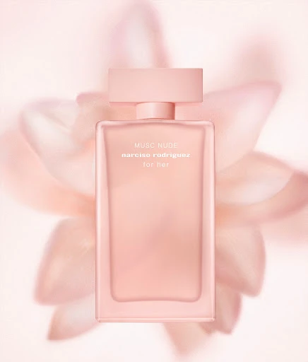 Close-up product shot of a peach-toned Narciso Rodriguez Musc Nude perfume bottle set against a blurred pale peach floral backdrop.
