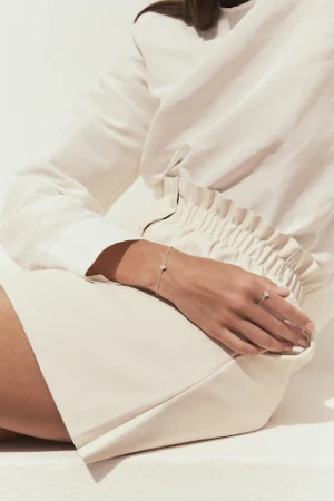 Close-up of a person wearing a delicate silver bracelet and ring, styled by Helene Leverrier against a light background.