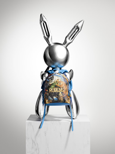 Metallic bunny sculpture on a white marble block with a small printed backpack against a plain gradient white background.