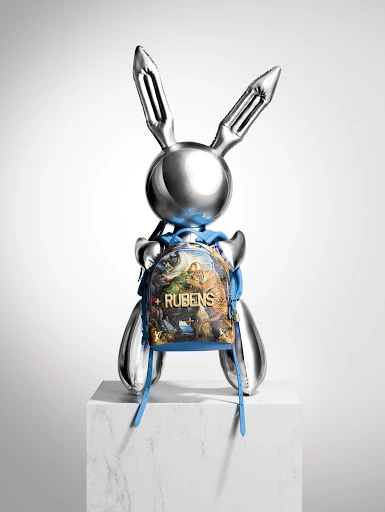 Metallic bunny sculpture on a white marble block with a small printed backpack against a plain gradient white background.