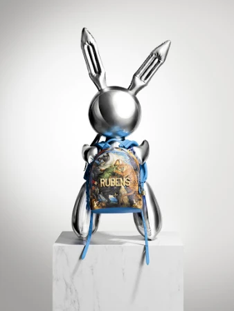 Metallic bunny sculpture on a white marble block with a small printed backpack against a plain gradient white background.