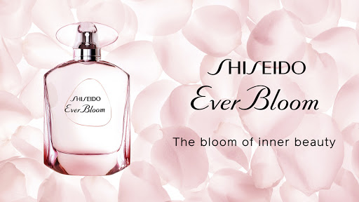Elegant, translucent pink perfume bottle featuring Shiseido Ever Bloom logo, set against a backdrop of soft, blurred flower petals.