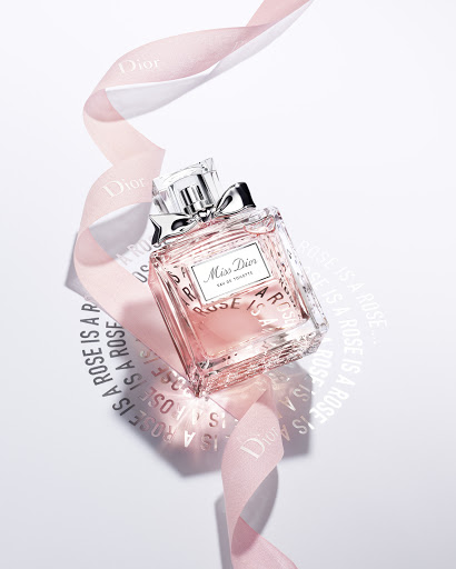 Miss Dior perfume bottle, adorned with a ribbon, sits on a white surface with shadow lettering; a beauty product shot for marketing.