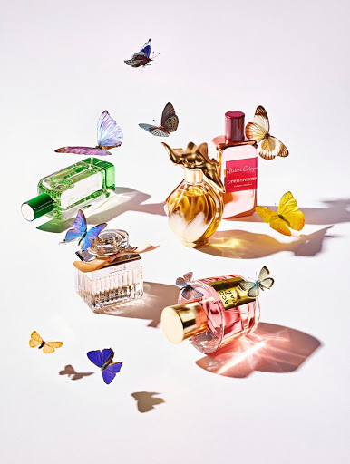 Several perfume bottles of different colors and shapes are arranged on a white surface, adorned with delicate butterflies.