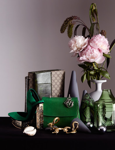 Still life of luxury fashion accessories and objects: a handbag, high heel shoe, floral arrangement, and decorative objects.