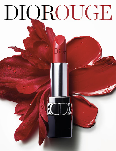 Close-up of Dior lipstick in a silver tube with red flower petals and red lipstick smear on a white background, beauty shot.