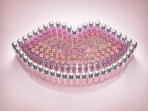 Arrangement of numerous lipstick tubes forming the shape of a pair of lips against a soft pink gradient background.