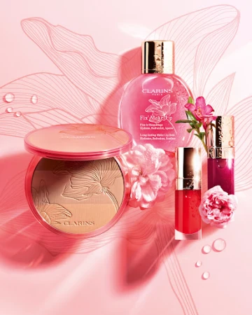 Clarins Fix Make-Up setting spray, lip gloss and bronzer compact with botanical accents on a soft pink gradient surface.