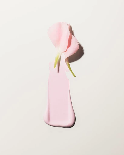 Pink flower petal atop a smooth pale pink cosmetic swatch on a neutral background by set designer Helene Leverrier