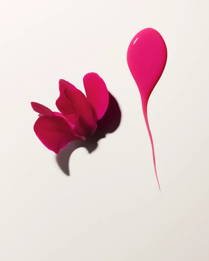 Vibrant pink orchid blossom next to a glossy liquid paint drop with a trailing tail on a white seamless background