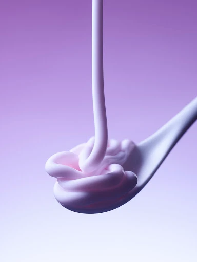 White cosmetic cream pouring onto a white spoon against a smooth purple gradient background