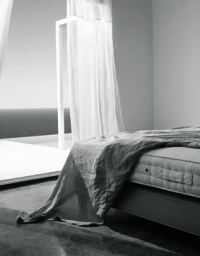 Black and white bedroom interior with a made bed, draped sheer curtains, and an open doorway overlooking the sea.