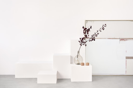 Minimalist still life featuring a glass vase with a branch, two wicker balls, and an abstract painting, all in soft, neutral tones.