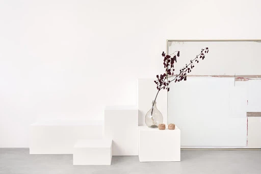 Minimalist still life featuring a glass vase with a branch, two wicker balls, and an abstract painting, all in soft, neutral tones.