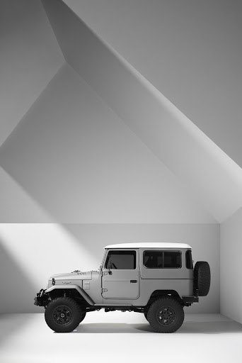 Profile shot of a classic gray Toyota Land Cruiser against a studio backdrop featuring strong geometric shadows and white walls.