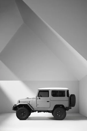 Profile shot of a classic gray Toyota Land Cruiser against a studio backdrop featuring strong geometric shadows and white walls.