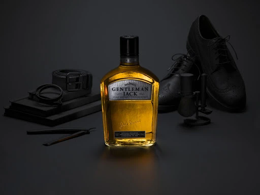 Studio shot of Jack Daniel's Gentleman Jack whiskey bottle with black leather dress shoes, shaving brush, and straight razor.