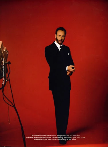 Tom Ford in a black suit poses in front of a red backdrop, captured in a studio setting with soft lighting and a classic portrait style.