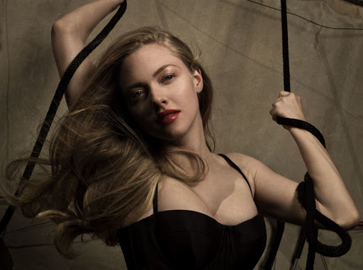 Amanda Seyfried portrait with dramatic lighting, dark corset, flowing blonde hair, holding dark rope, photographed in a studio with neutral background.