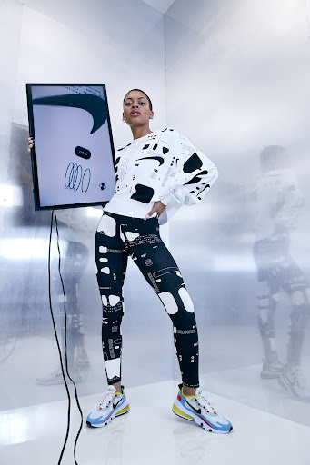Adult female fashion model posing in a photo studio wearing athletic leggings, a sweatshirt, and sneakers and holding a framed image.