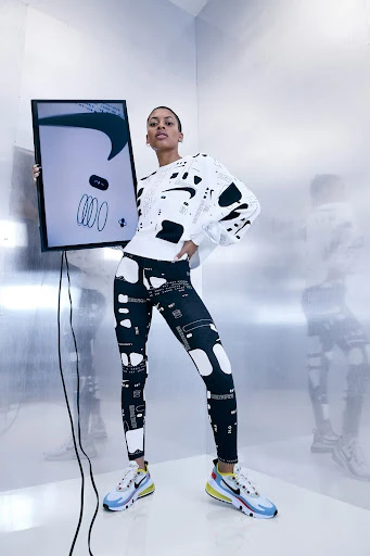 Adult female fashion model posing in a photo studio wearing athletic leggings, a sweatshirt, and sneakers and holding a framed image.