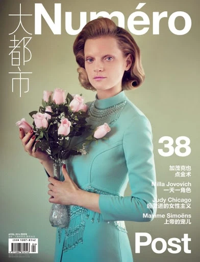 Magazine cover featuring a fair-skinned woman in a light blue dress holding light pink roses against a soft green background. Title: Numero.
