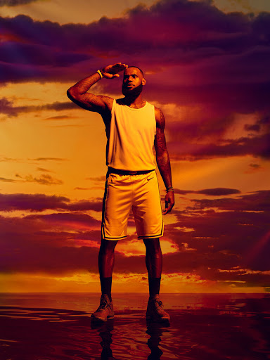 Basketball player LeBron James poses outdoors in athletic wear. He is looking towards the horizon with an orange sky in the background.