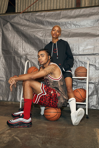 Two models in a casual pose on a basketball court, showcasing sneakers and streetwear, with basketballs as props against a silver backdrop.