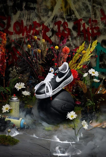 Artistic still life featuring a Nike sneaker balanced on a basketball, spray paint cans, and flowers against a graffiti background.