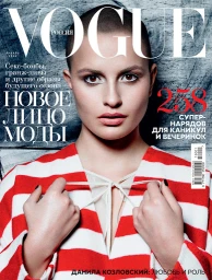 Close-up portrait of a model with a shaved head wearing a red and white striped sweater against a textured grey wall
