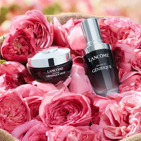 Lancome Advanced Genifique serum and eye cream sit among pink rose petals in a visually appealing beauty still life product shot.