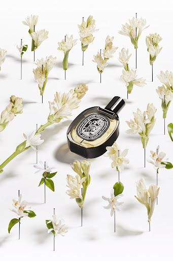 Elegant studio shot of a perfume bottle surrounded by fresh white flowers pinned to a white surface, showcasing beauty and floral fragrance.