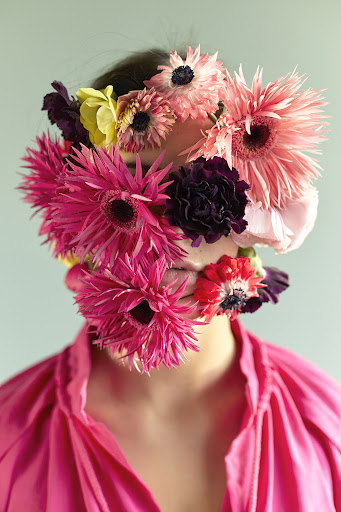 Portrait of a person wearing a vibrant pink shirt with a dense arrangement of colorful flowers covering their face.