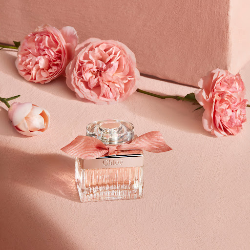 Chloe perfume bottle on a pink surface with pink roses. Close-up shot of perfume bottle with bow and flowers against pink background.