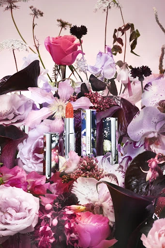 Floral arrangement featuring Givenchy lipstick in silver tubes with floral designs, showcasing beauty and fashion in an indoor studio setting.