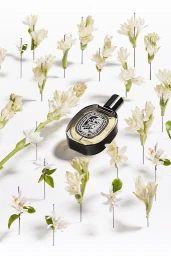 A perfume bottle surrounded by white flowers pierced with pins on a white background