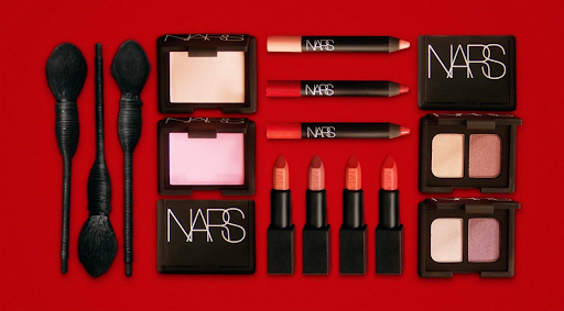 NARS makeup arranged symmetrically on a red background, featuring brushes, palettes, lipsticks, and crayons for beauty product visuals.