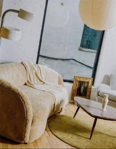 Interior design featuring a tan sofa with a throw blanket, set on a wooden floor with a modern coffee table and minimalist decor.