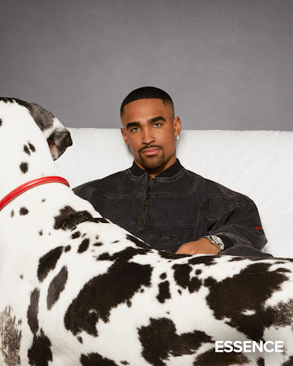Portrait of an adult male sitting on a white couch next to a Great Dane dog in a photo studio against a solid grey backdrop.