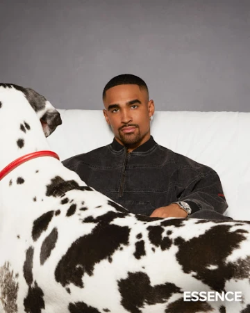 Portrait of an adult male sitting on a white couch next to a Great Dane dog in a photo studio against a solid grey backdrop.